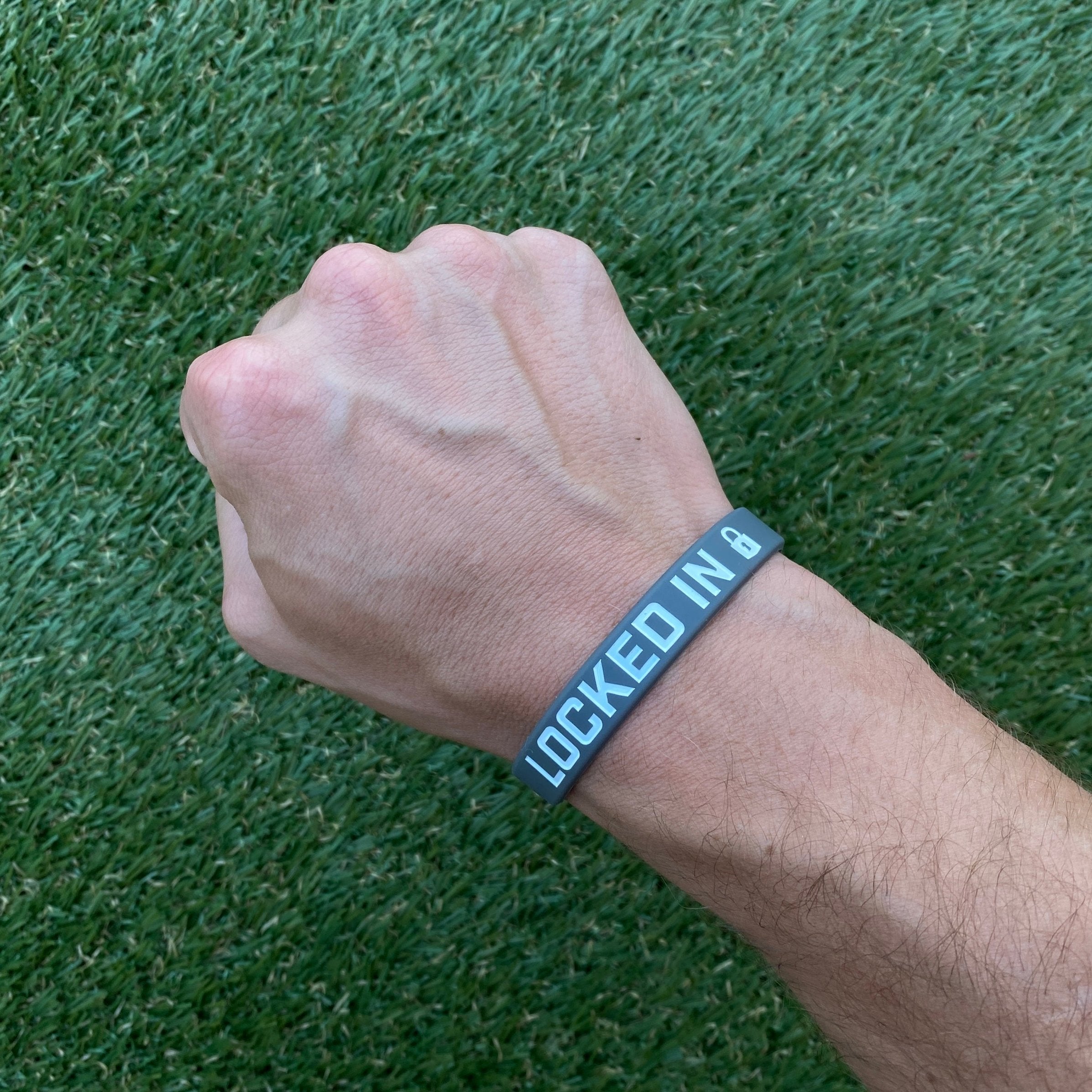 Collection of Hand wearing a wristband with 'LOCKED IN' text on a grass background in a gallery layout